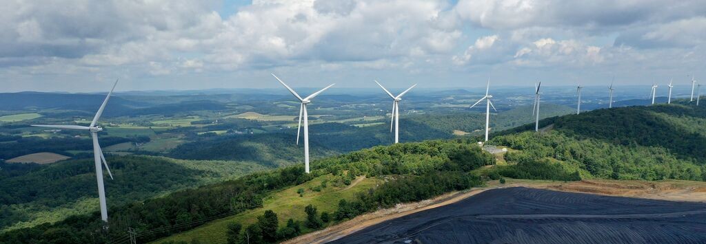 Wind turbines generating renewable energy on a reclaimed mining landscape surrounded by rolling green hills under a partly cloudy sky.