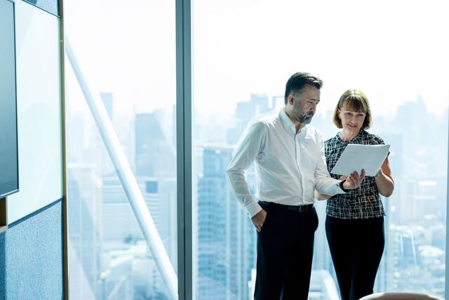 Two professionals review a document in a modern office with large windows overlooking a city skyline.